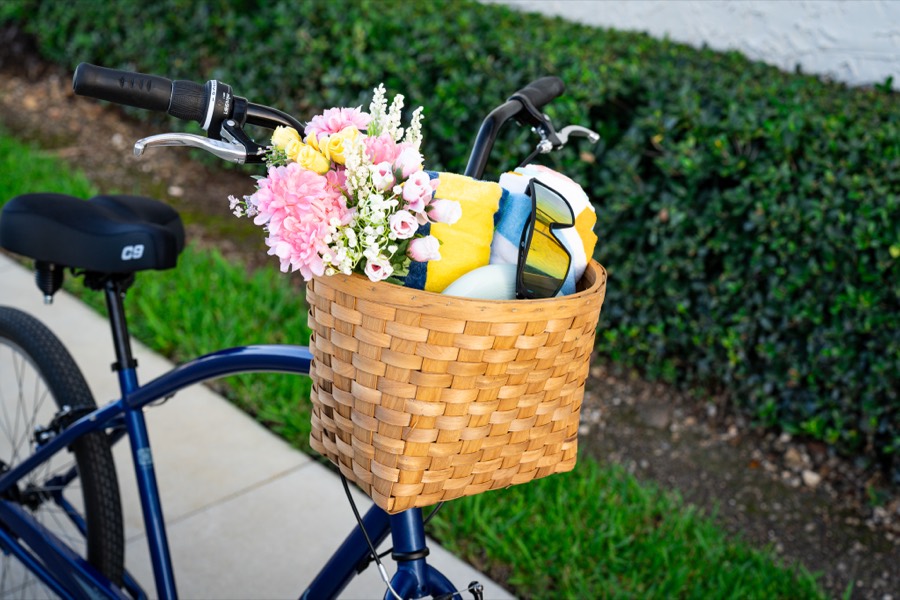 A Sunlite woven wooden basket on a cruiser handlebar, packed with flowers and a beach towel.